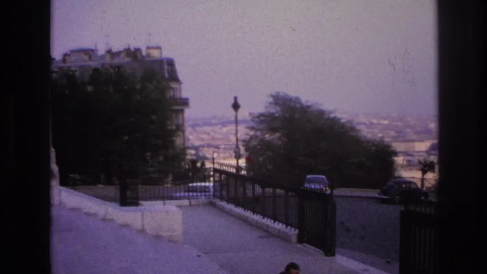 1967 Paris travel footage showing an elevated approach with black railings, roadside cars, trees, and a hazy spread of city rooftops.