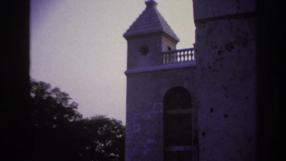 1967 Paris 8mm frame showing a pale stone tower, arched opening, conical roof, and trees through a dark architectural frame.