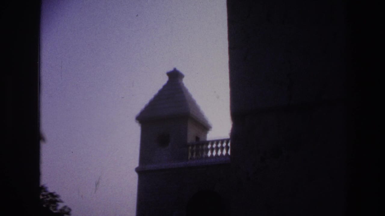 1967 Paris 8mm frame with the tower partly hidden by a dark foreground edge, showing the roof, balcony rail, sky, and masonry.