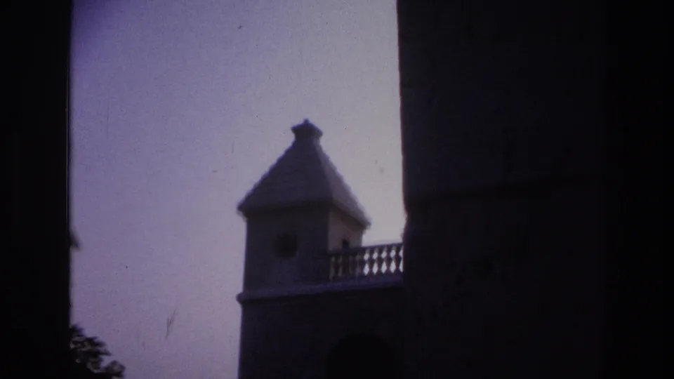 1967 Paris 8mm frame with the tower partly hidden by a dark foreground edge, showing the roof, balcony rail, sky, and masonry.