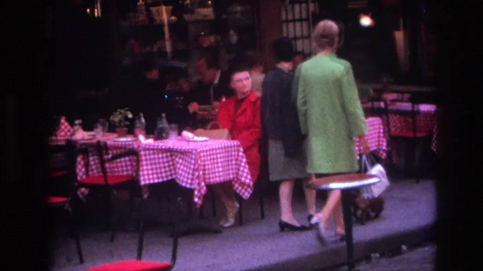 Near the end of the clip, the women pass close to Paris cafe tables where diners sit under dim light beside a small dog near the curb.