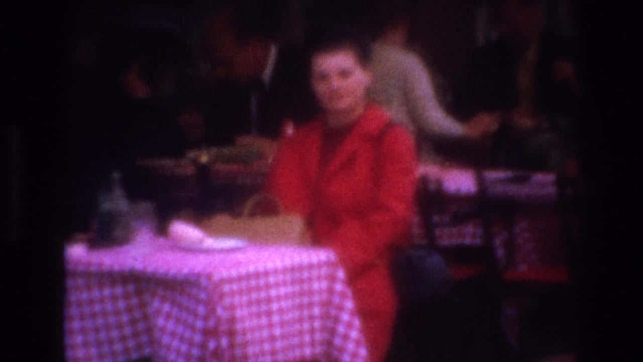 Soft-focus view of a woman in a red coat beside a checkered cafe table in a crowded setting.