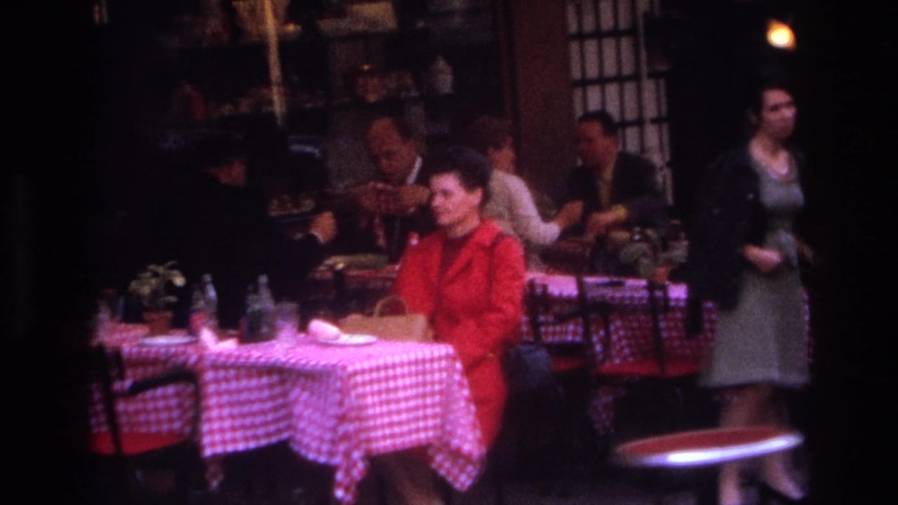 1967 Paris outdoor cafe scene with checkered tablecloths, seated patrons, and a woman in a red coat near the foreground.
