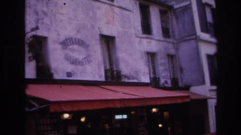 1967 Paris street frontage with the patisserie sign, red awning, apartment windows, and darkened bakery entrance below.