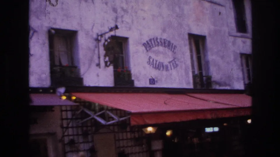 1967 Paris patisserie exterior with a red awning, faded wall lettering, residential windows, balcony plants, and shopfront details.