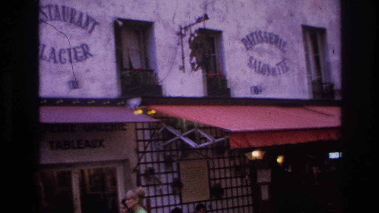 1967 Paris home-movie frame showing French cafe or restaurant signage, red awnings, windows, and a partial sidewalk view.