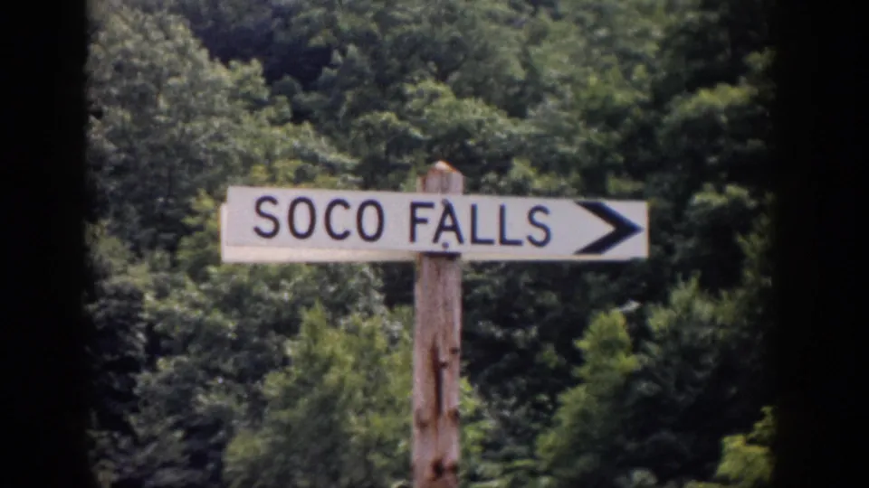 Wooden SOCO FALLS directional sign with an arrow, filmed against a wooded hillside in the 1959 home-movie clip.