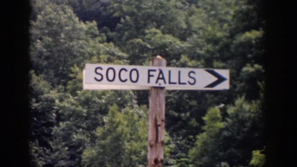 Closer 8mm view of the SOCO FALLS arrow sign on a wooden post, with leafy forest filling the background.