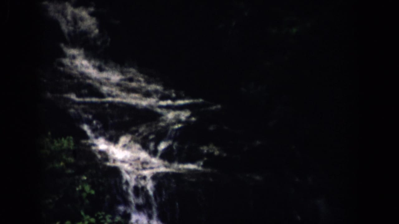1959 Colorado 8mm frame showing white water cascading over dark, wet rock ledges with foliage at the edge.