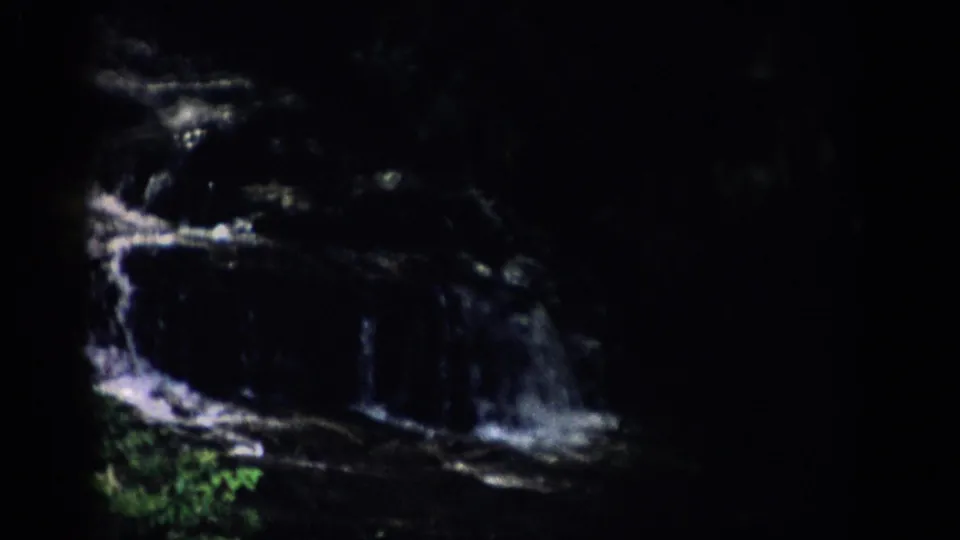 1959 Colorado 8mm frame showing the lower cascade of a small waterfall beside green foliage and shadowed rock.