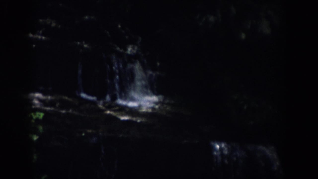 1959 Colorado 8mm frame showing bright water cascading over dark rock ledges in a shaded wooded stream.
