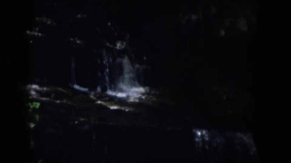 1959 Colorado 8mm frame showing bright water cascading over dark rock ledges in a shaded wooded stream.