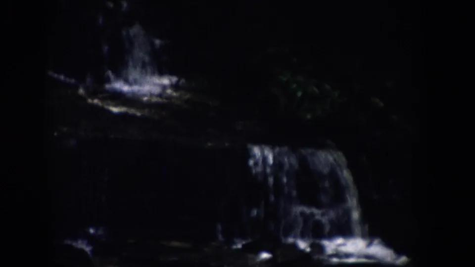 A low-light 1959 Colorado frame shows several small cascades stepping across dark rocks in a wooded stream.