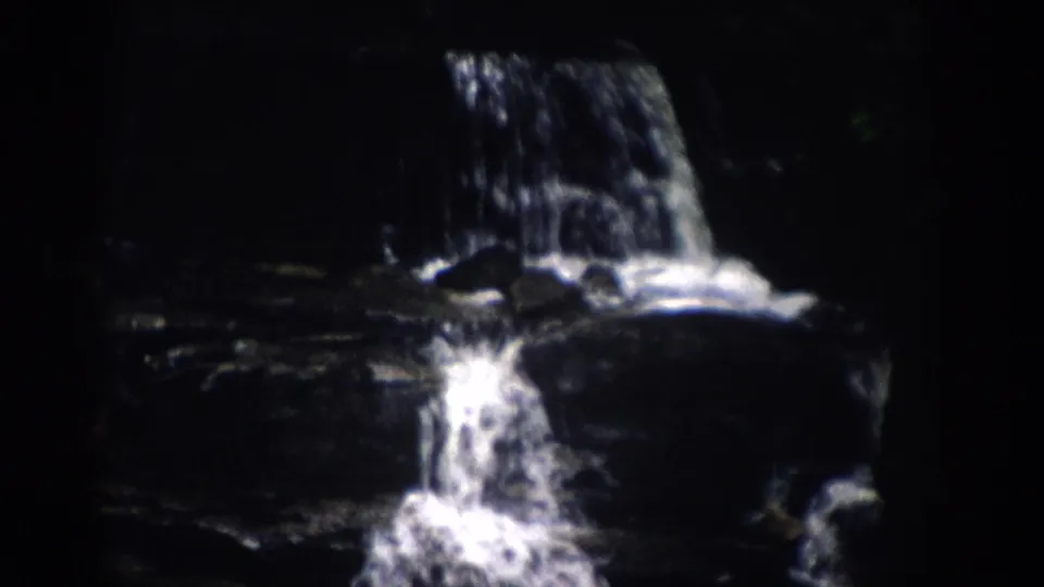 A 1959 Colorado home-movie frame shows two small rock cascades with white splashes against deep shadows.