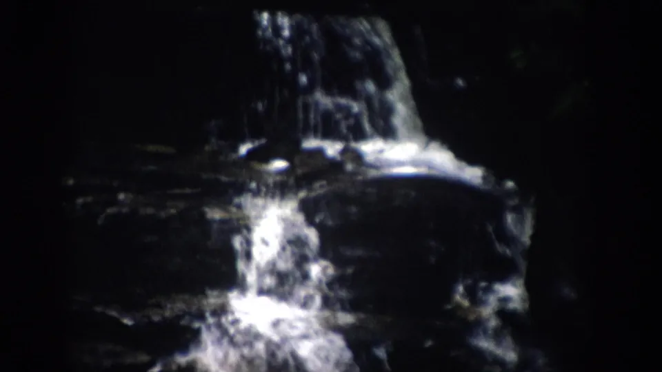 1959 Colorado 8mm frame showing white water falling over dark rock ledges in a shaded wooded preserve.