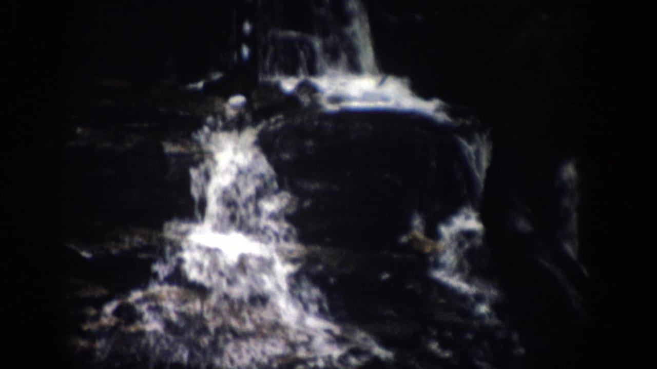 Waterfall and wet rock ledges framed by heavy shadow.