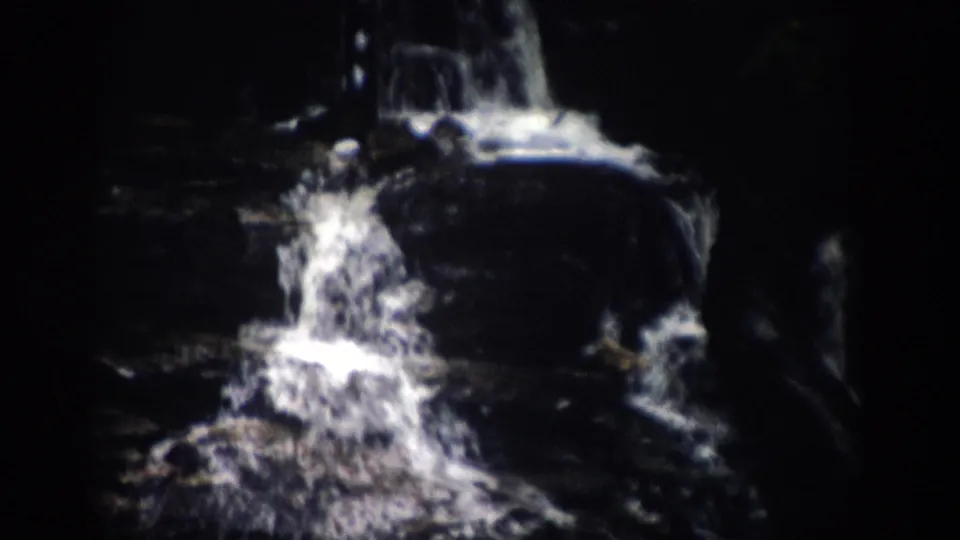Archival 8mm view of a Colorado waterfall with bright spray against dark rocks and surrounding woods.