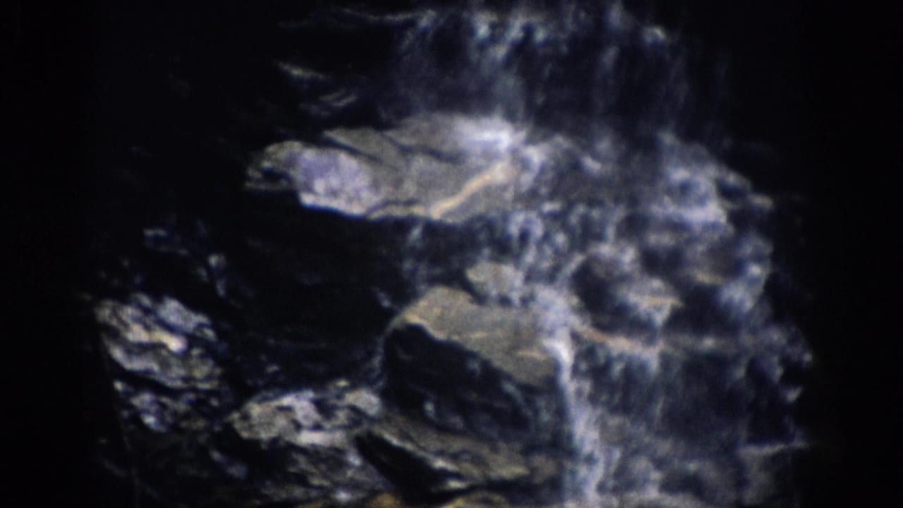 Water rushes over dark jagged rocks in a shadowed cascade.