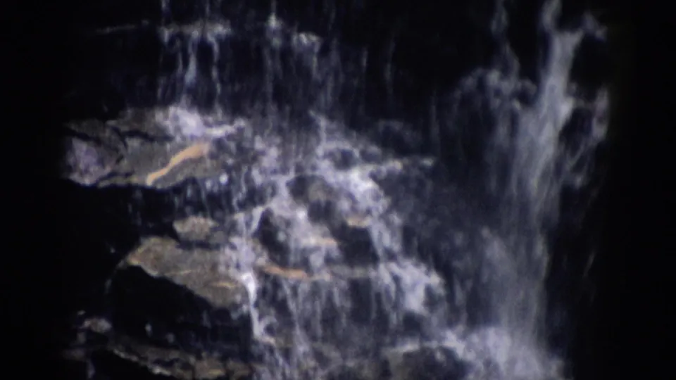 1959 Colorado 8mm frame showing a narrow waterfall dropping over layered rocks with bright spray.