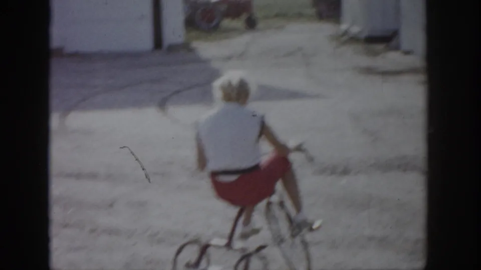 A child rides a red tricycle through a dusty yard in the 1959 Colorado home-movie footage.
