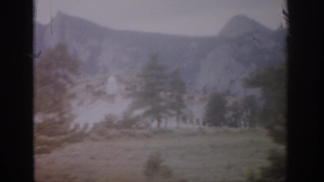 1959 Colorado 8mm frame showing hazy mountains, trees, open ground, and a pale building in a soft, faded home-movie view.