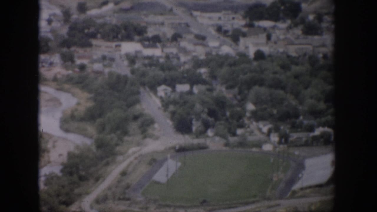 Aerial view of a small town with a winding river, roads, trees, and an athletic field.