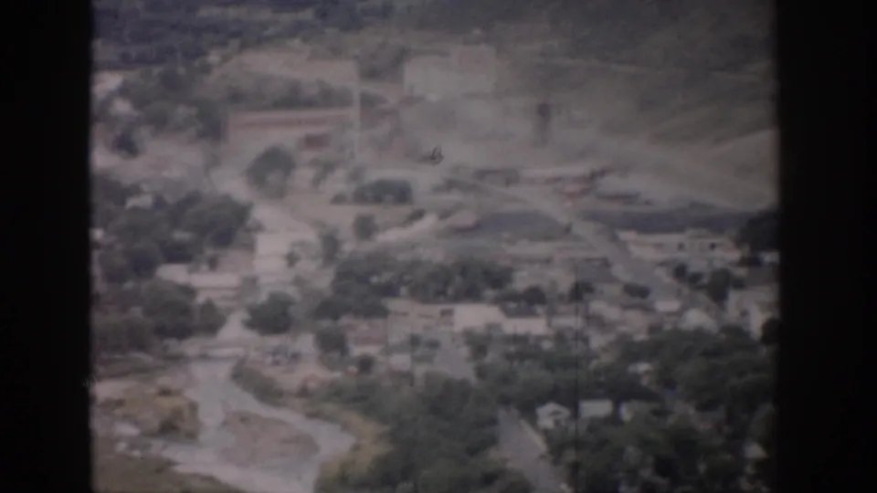 1959 Colorado aerial frame with curving roads, tree cover, scattered houses, and a larger rectangular building in the distance.