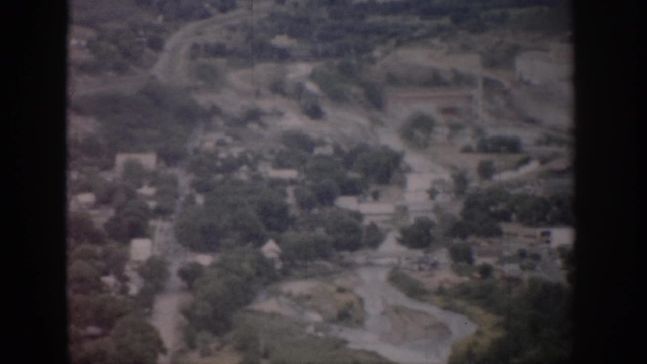1959 Colorado 8mm aerial view showing a small town, winding roads, tree cover, homes, and surrounding open land.