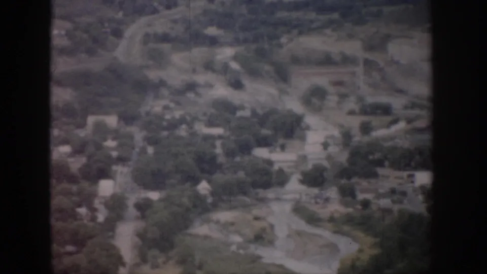 1959 Colorado 8mm aerial view showing a small town, winding roads, tree cover, homes, and surrounding open land.