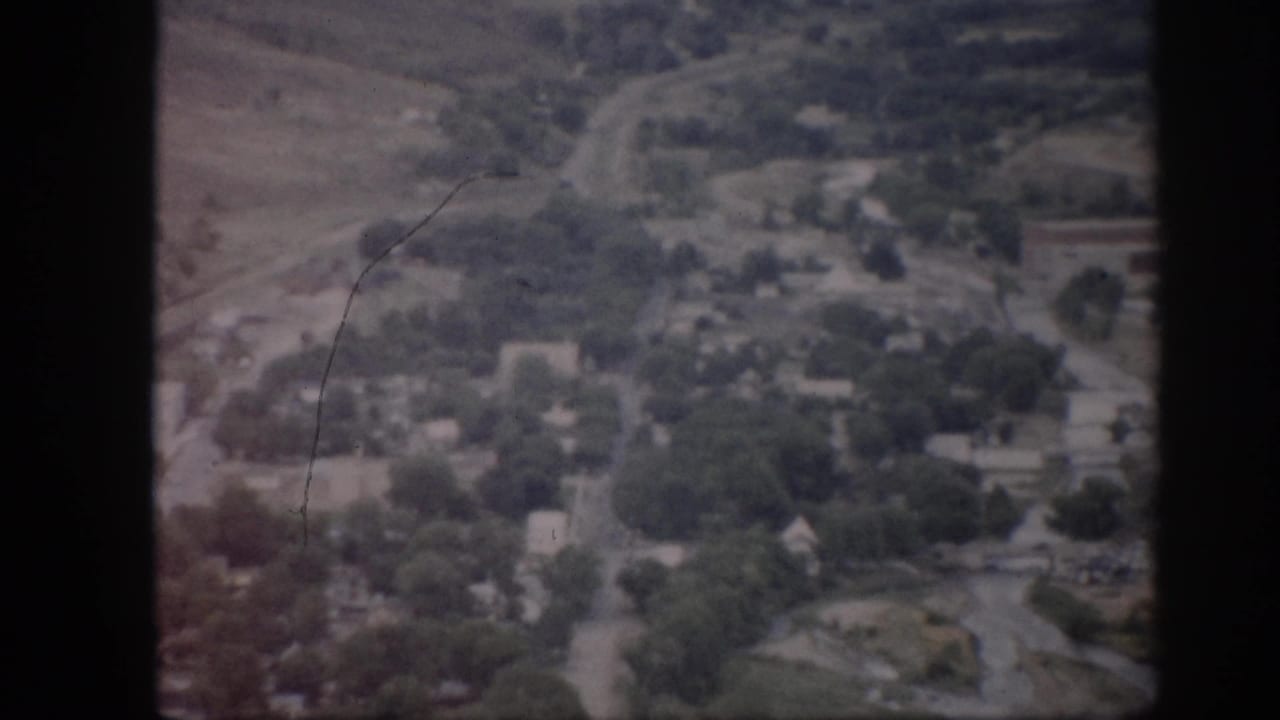 Aerial town view with roads, trees, houses, open land, and film scratches.
