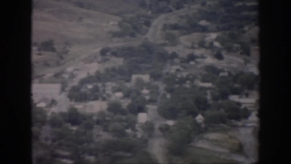 1959 Colorado 8mm aerial view looking down over a small town with roads, houses, tree cover, and surrounding fields.