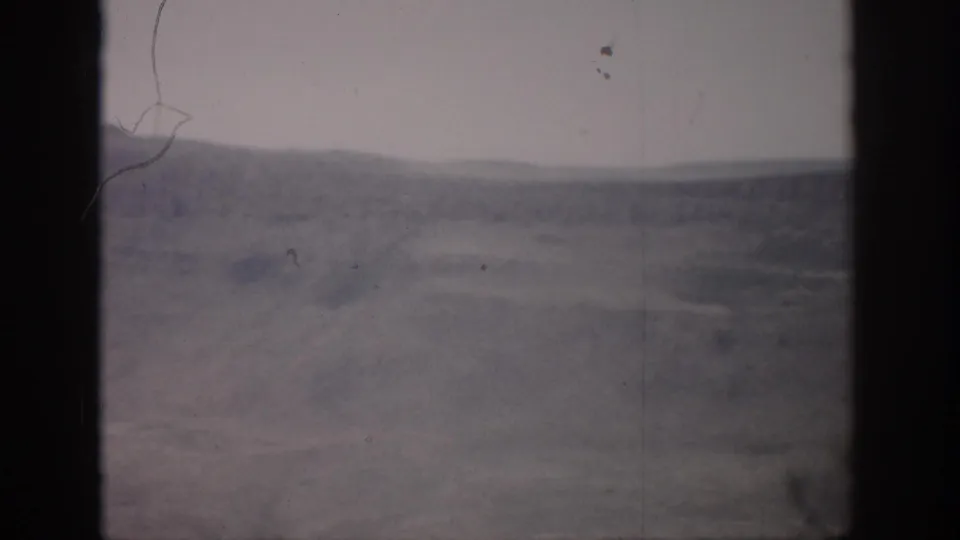 1959 Colorado 8mm frame showing a muted valley landscape, distant hills, pale sky, and visible film wear.