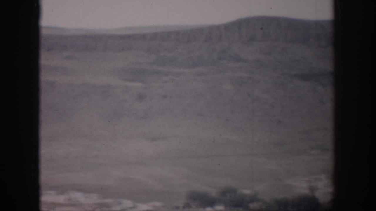 A soft 8mm view of a broad Colorado valley with rolling hills, sparse vegetation, and dark window borders.