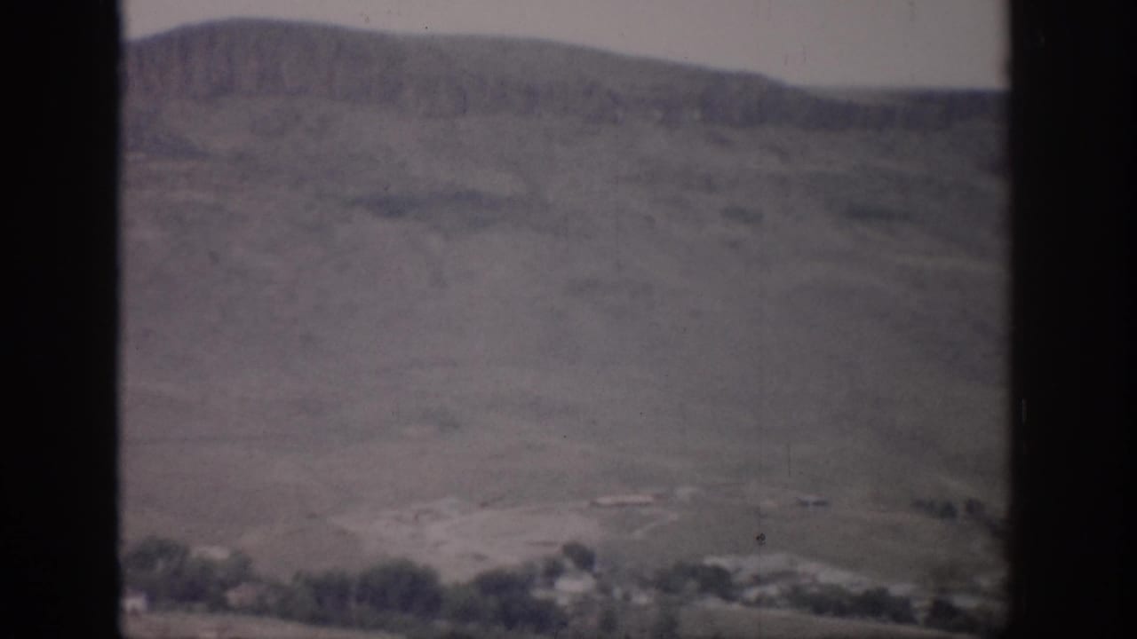 Muted hillside and valley floor with scattered structures below.