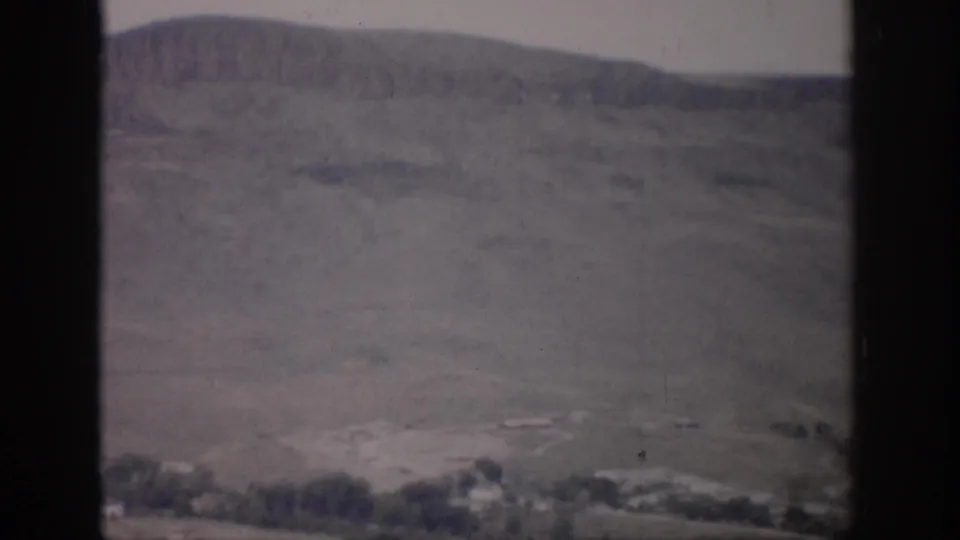 1959 Colorado home-movie view across a muted hillside toward a small settlement on the valley floor.