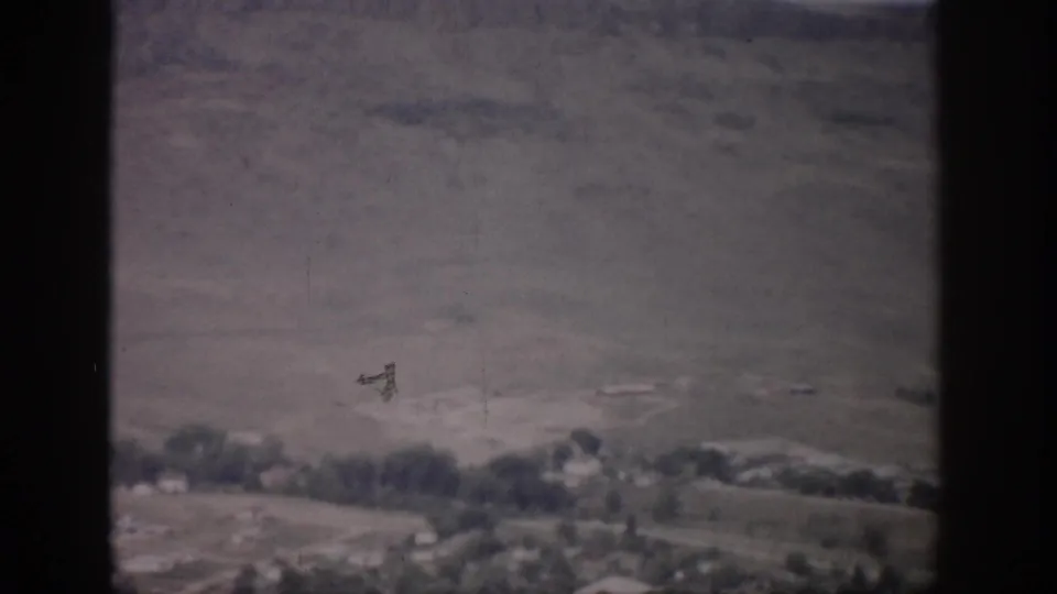 Soft 8mm frame of a Colorado valley town below dry hills, with trees and pale ground visible in the distance.