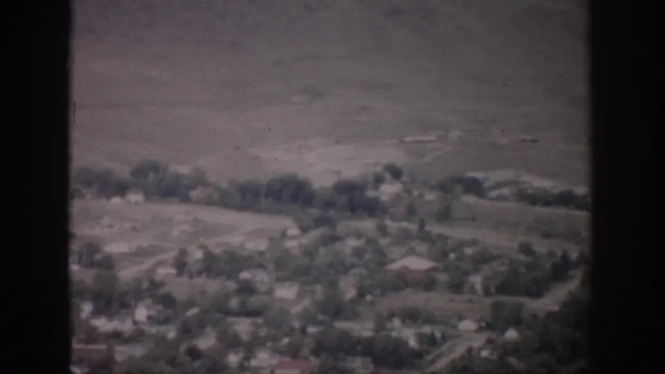 1959 Colorado frame showing a tree-dotted settlement, faint roads, and a dry hillside beyond the valley.