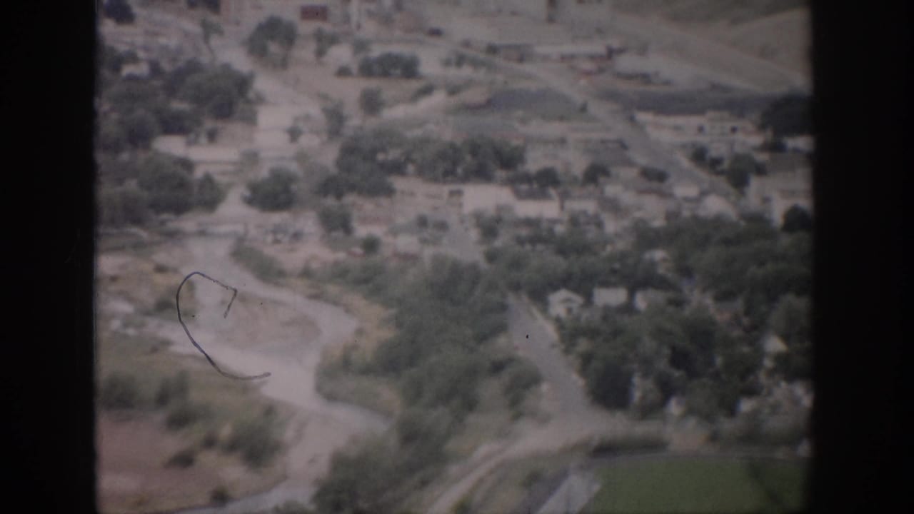 Aerial view of a pale river bend, roads, trees, houses, and open land.