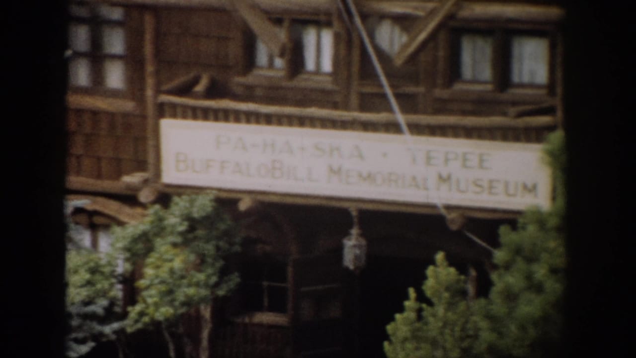 1959 Colorado home-movie view of the Buffalo Bill Memorial Museum sign on a rustic wood building, partly obscured by trees.