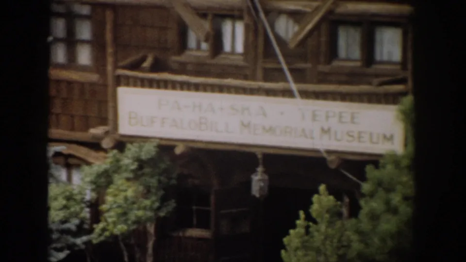 1959 Colorado home-movie view of the Buffalo Bill Memorial Museum sign on a rustic wood building, partly obscured by trees.