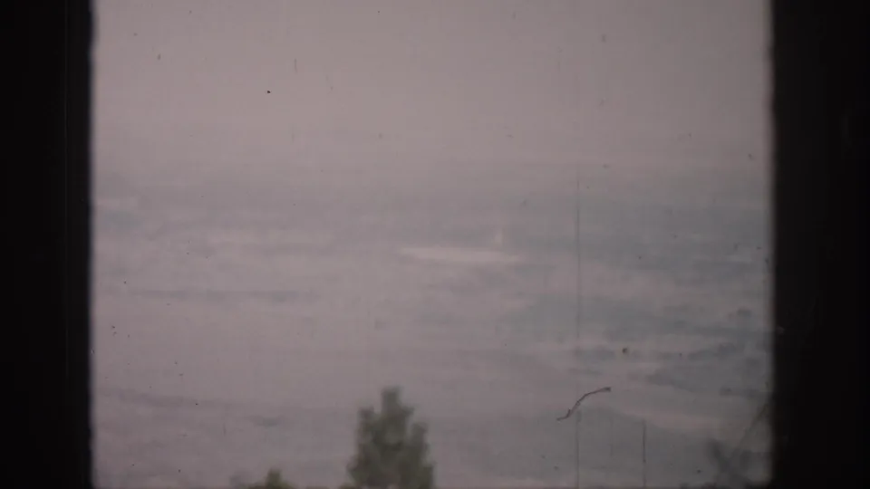 1959 Colorado 8mm landscape view through dark window framing, with faint trees, hazy terrain, and visible film wear.