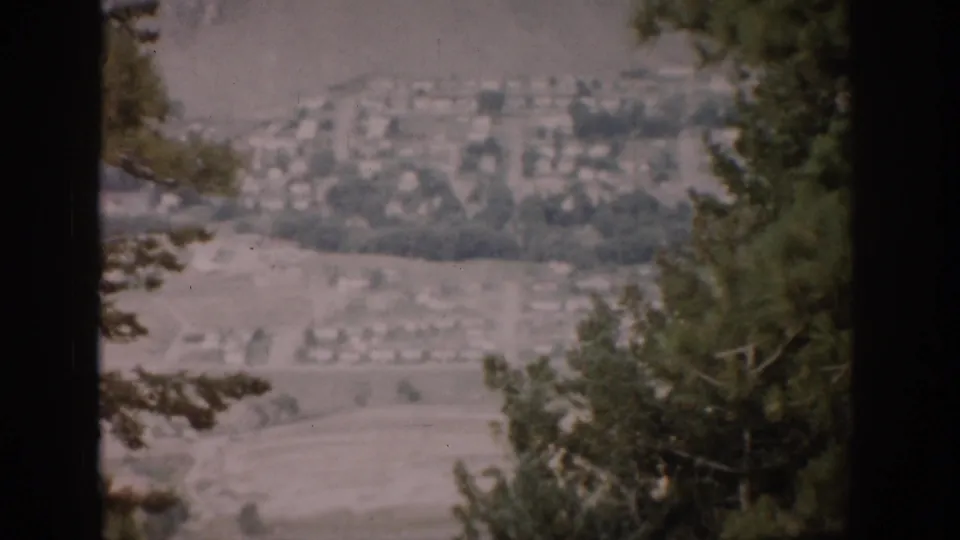 Tree-framed 1959 Colorado valley view with houses and open land visible in soft 8mm color.