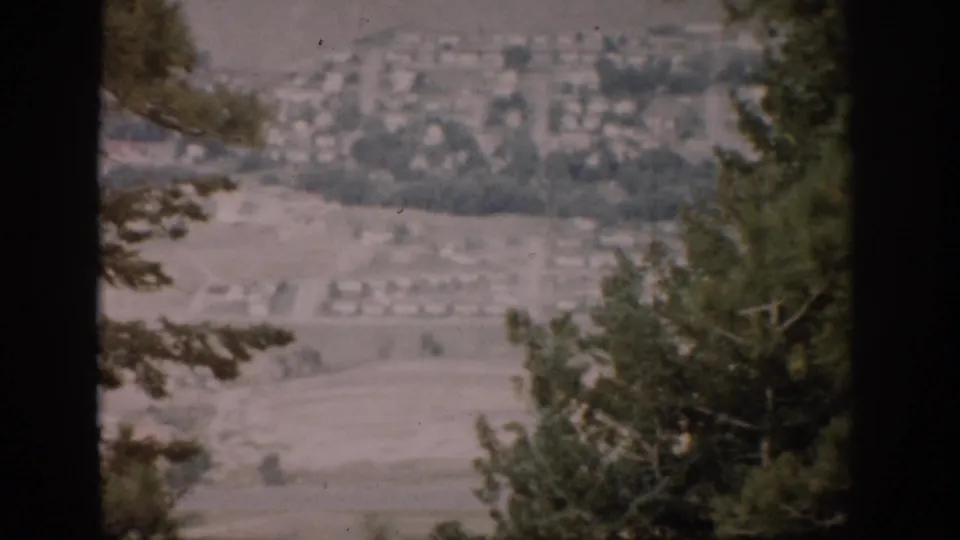 Faded 1959 Colorado home-movie view of a valley neighborhood partly obscured by evergreen trees.