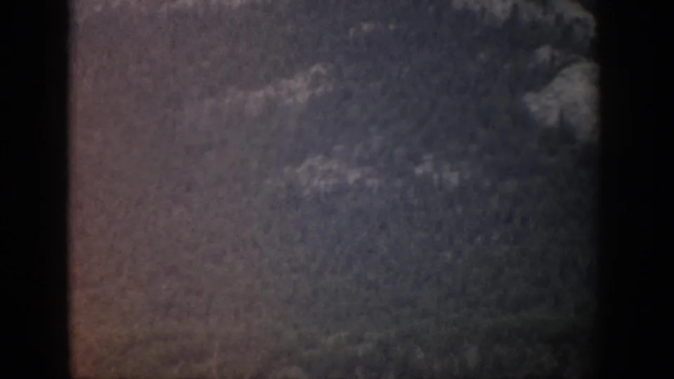 Darker 1959 Colorado 8mm frame showing a soft view of forested mountain slopes and a dark window border.