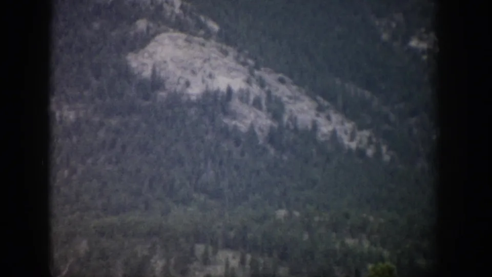Colorado mountain landscape on 8mm film, with a pale rocky ridge and surrounding forest in soft focus.
