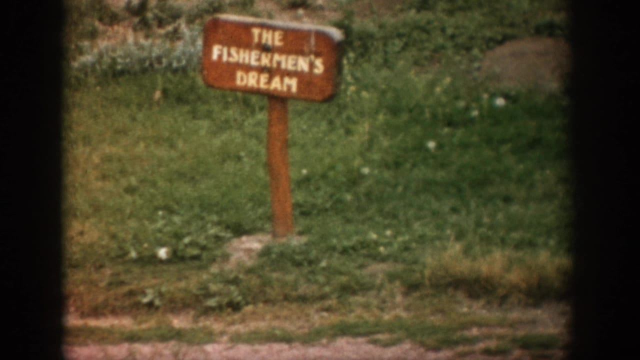 1959 Colorado 8mm frame with the The Fishermen's Dream sign centered near grass, rocks, and a dirt roadside edge.
