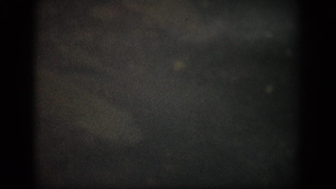 1959 Colorado 8mm frame showing murky shallow water through dark film edges, with faint underwater forms and visible grain.