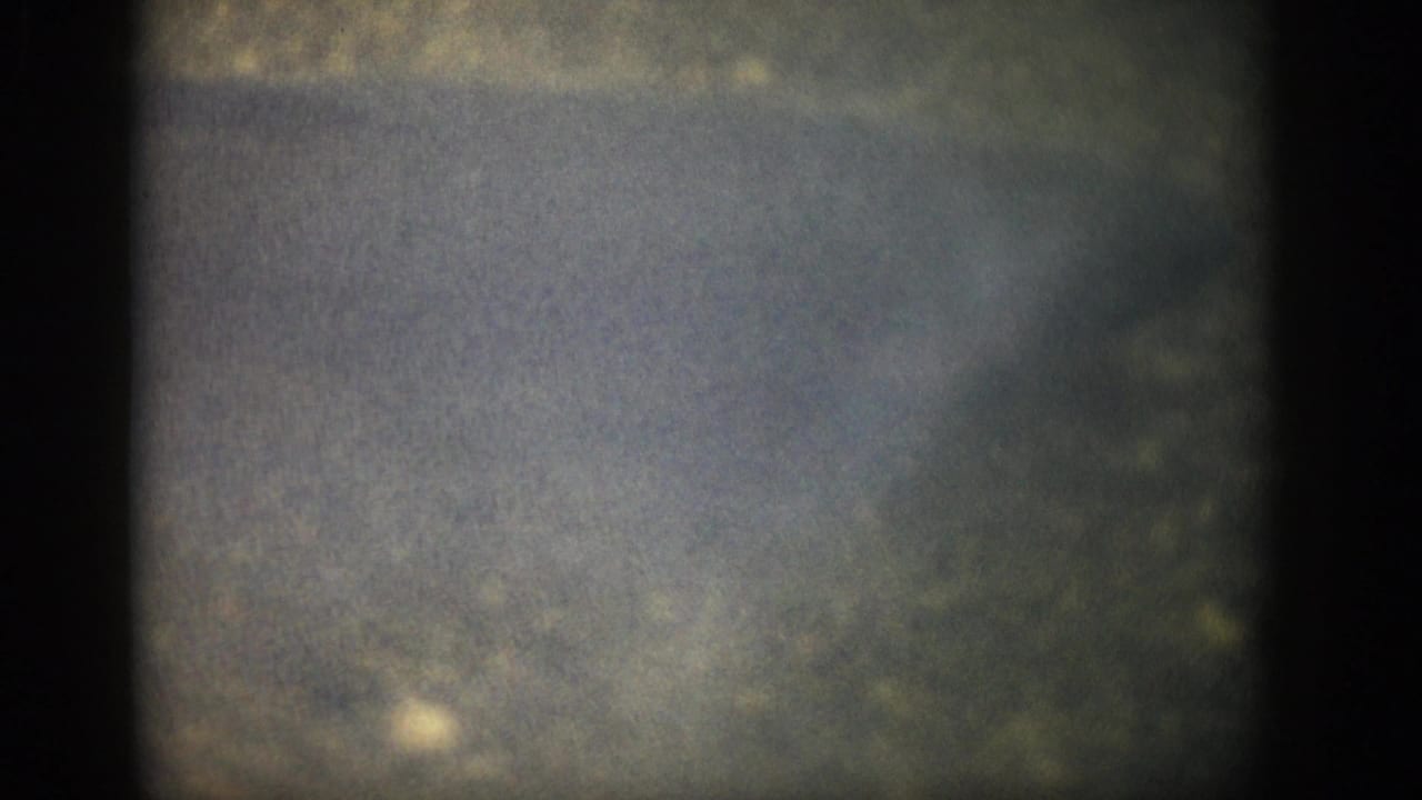 1959 Colorado 8mm frame showing murky shallow water, indistinct bank texture, film grain, and dark edge vignetting.