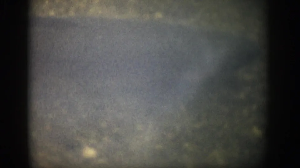 1959 Colorado 8mm frame showing murky shallow water, indistinct bank texture, film grain, and dark edge vignetting.