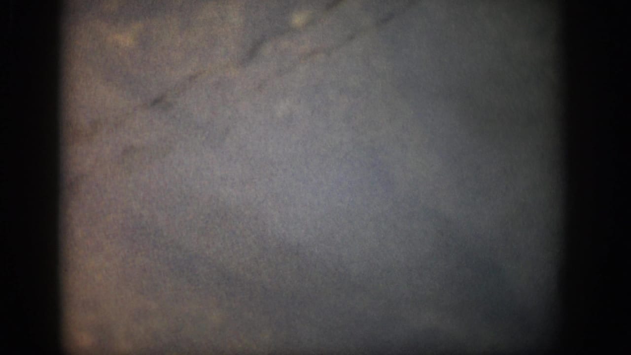 Opening 8mm frame from the Colorado 1959 clip showing mostly dark, mottled exposure before the stream scene appears.